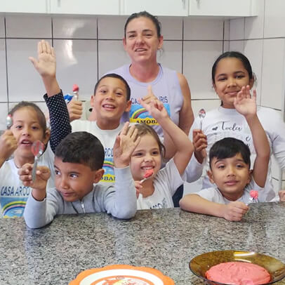 Imagem da cozinha com crianças e uma mulher adulta rindo posando para a foto com as mãos levantadas
